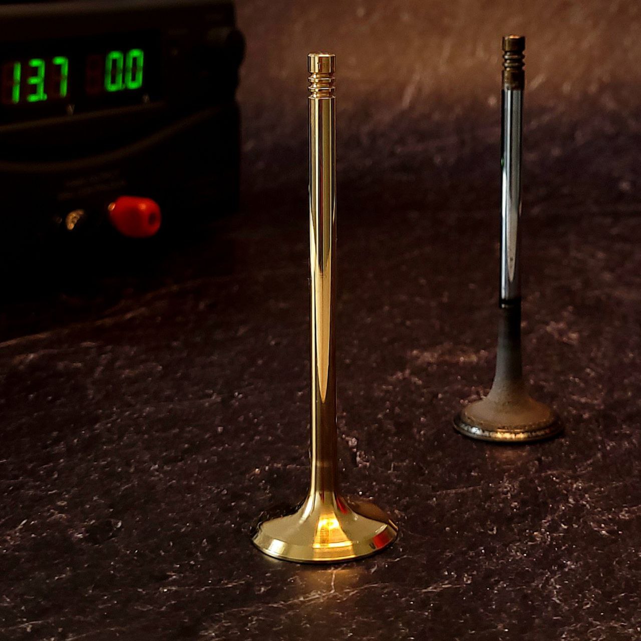Ein außergewöhnliches Souvenir. Als Basis dient ein sorgfältig aufbereitetes Einlassventil aus einem gebrauchten M52 BMW-Motor. Das Ventil ist mit 18K vergoldet und einer Lasergravur „BMW FOREVER“ versehen. Ventil nach der Vergoldung stehend und ALT im Hintergrund stehend abgebildet