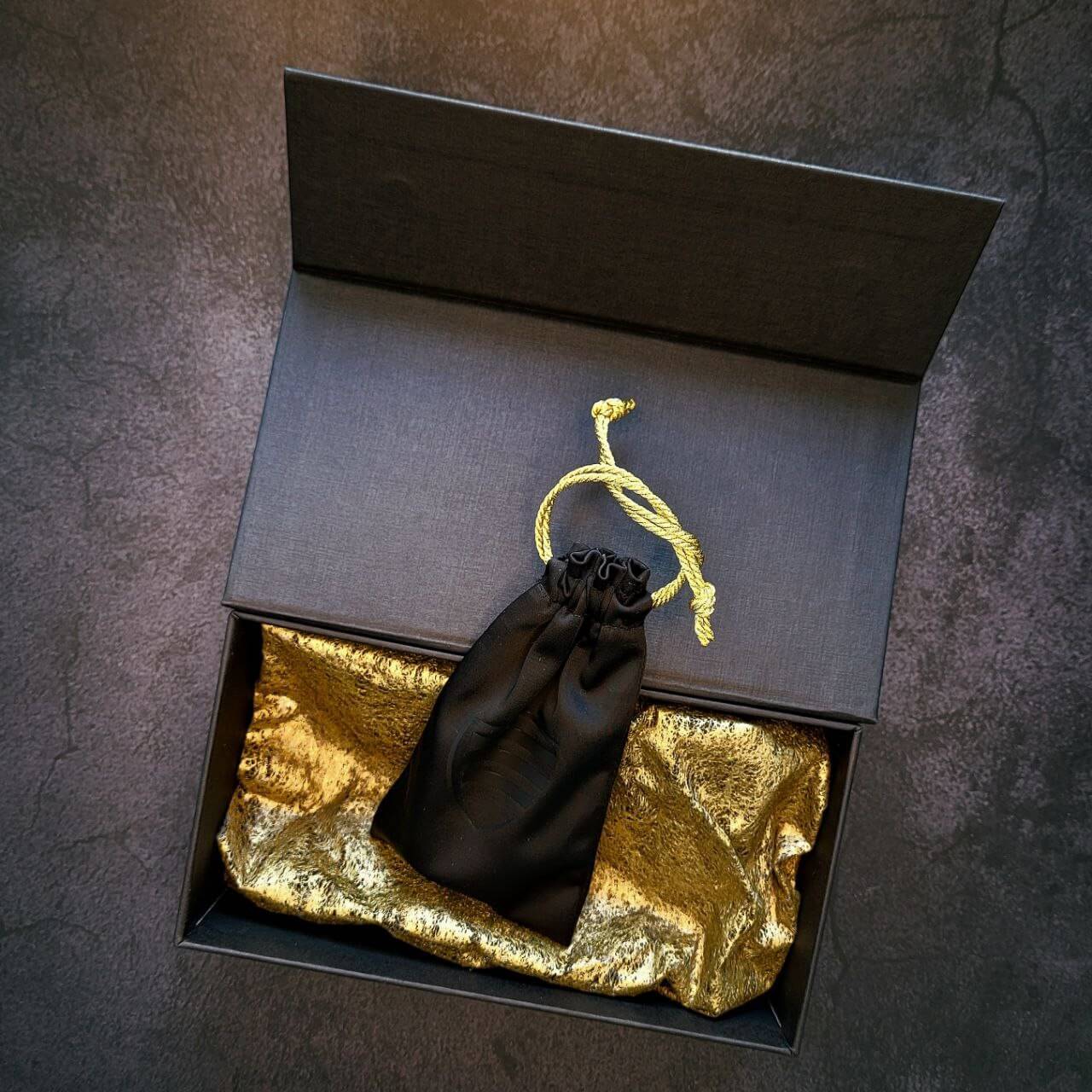 Ein außergewöhnliches Souvenir. Als Basis dient ein sorgfältig aufbereitetes Einlassventil aus einem gebrauchten M52 BMW-Motor. Das Ventil ist mit 18K vergoldet und einer Lasergravur „BMW FOREVER“ versehen. Das schwarze Säckchen liegend in der offenen Verpackung abgebildet