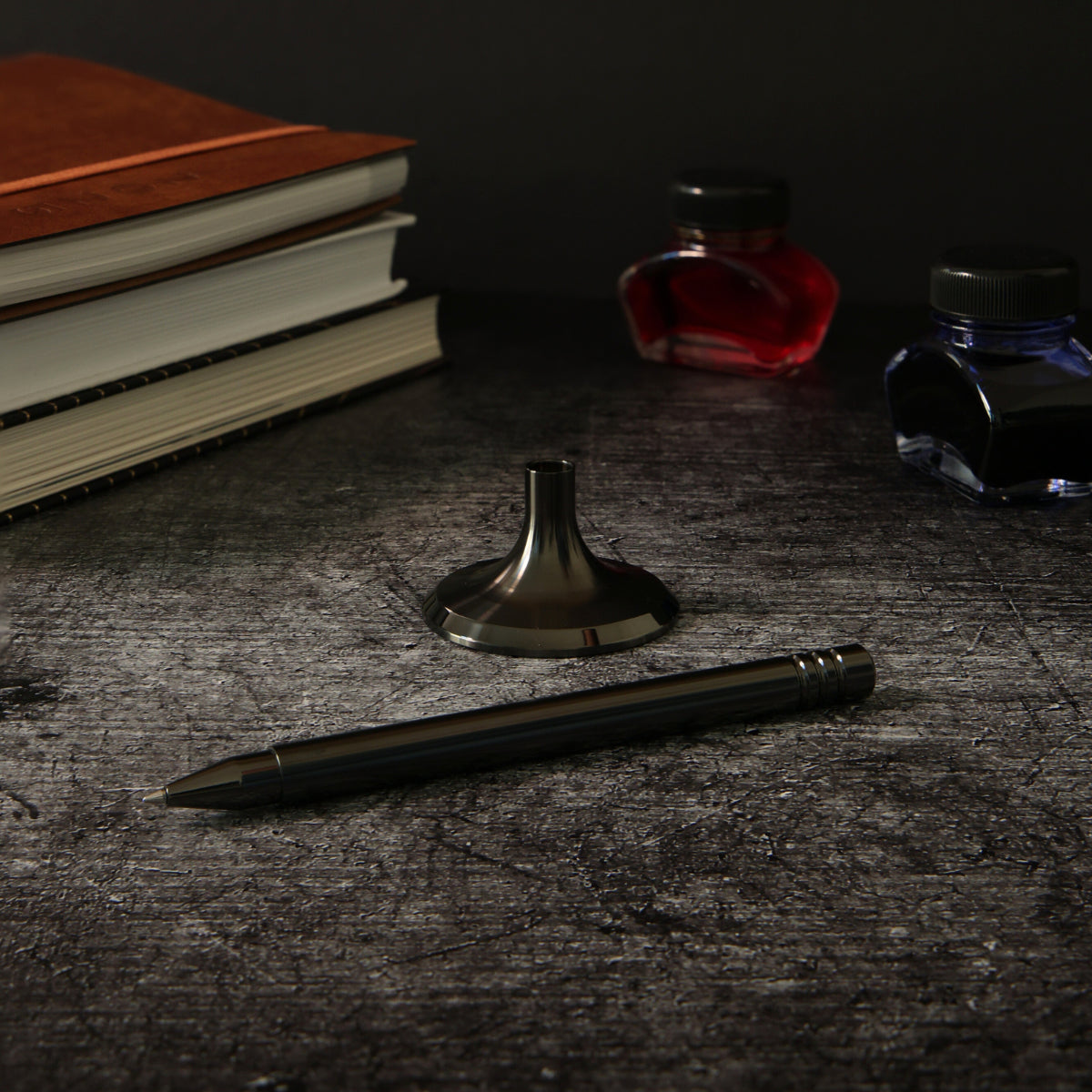 Ein elegantes Setup mit einem Tintenroller in DLC-_Anthrazit in einer abgedunkelten Umgebung. Im Hintergrund sorgen drei Bücher und zwei Fläschchen mit blauer und roter Tinte für eine stilvolle, romantische Atmosphäre.